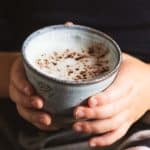 a small child holign a mug of babyccino with cocoa powder on top of the milk