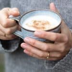 a woman holing a cardamom latte served in a ceramic cup
