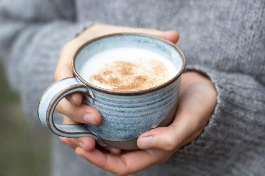 a woman holing a blue cermic mug of cardamom latte
