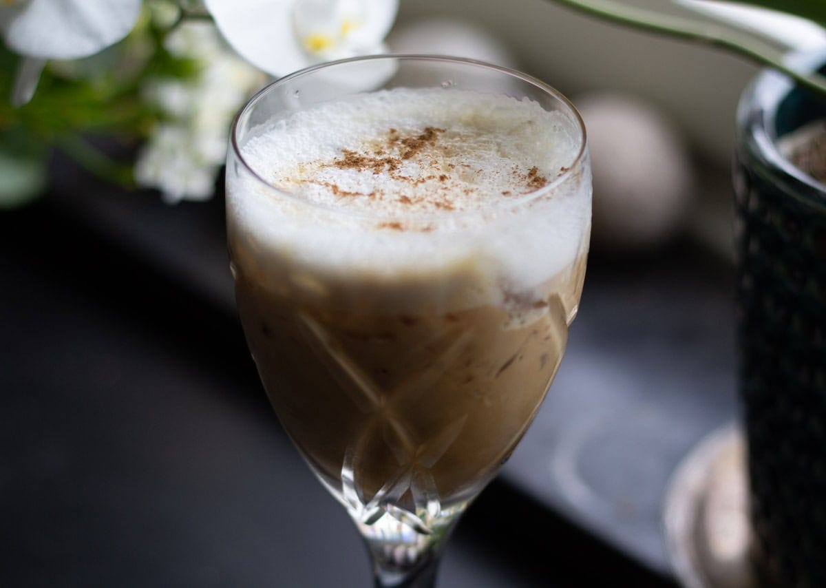 side view of a crystal glass filled with iced cardamom latte