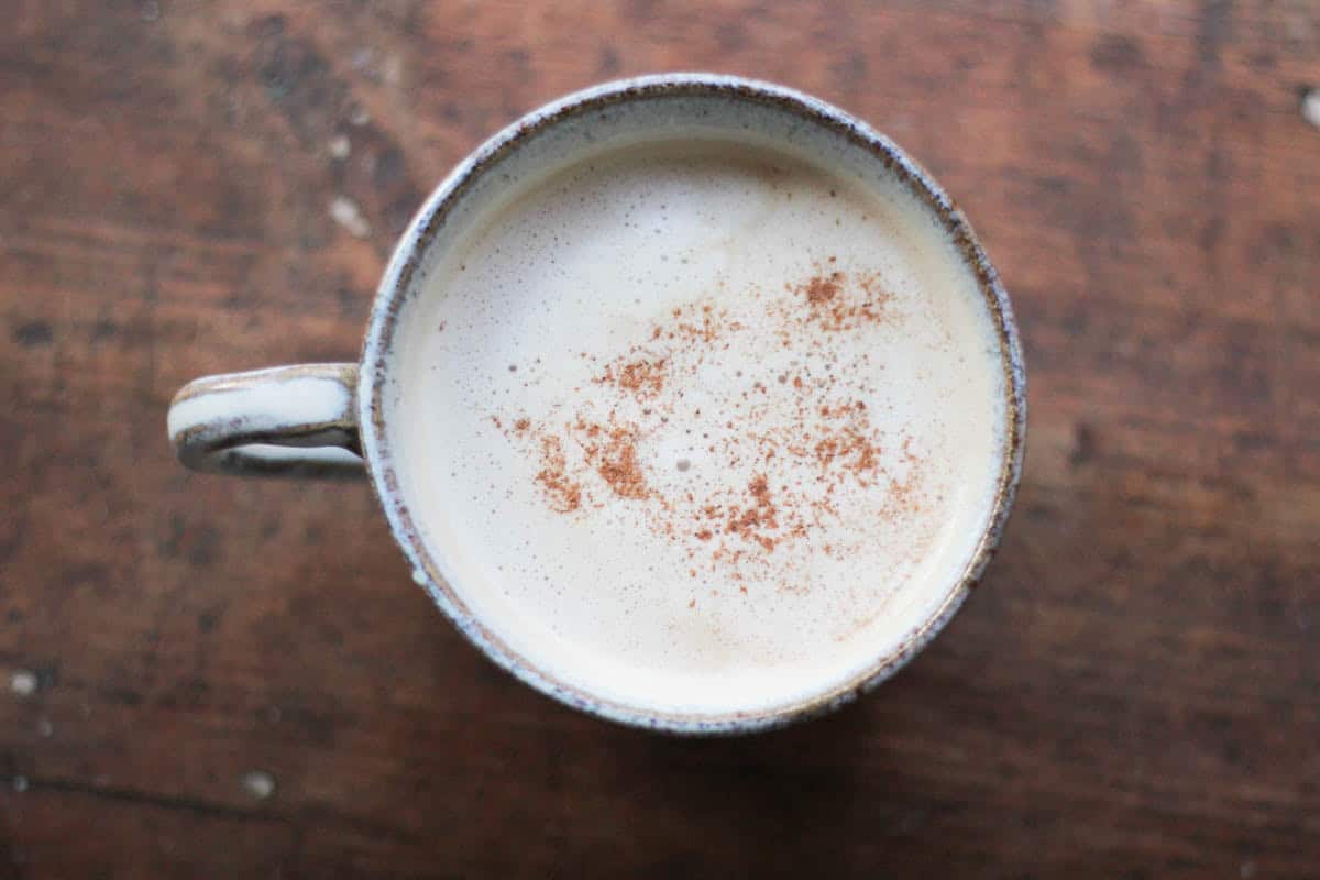 overhead view of a ceramic cup filled with cardamom latte and sprinkled with cocoa powder