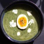 a cermaic bowl of nettle and wild garlic soup served with a drizzle of fresh cream and a sliced boiled egg