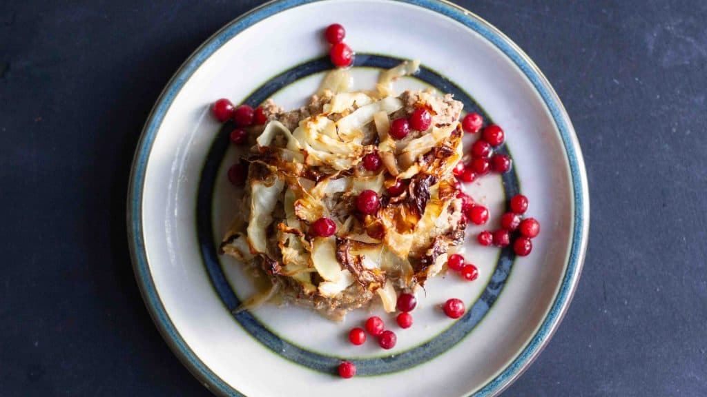 Caremlized Cabbage Meatloaf -Swedish Kålpudding served on a ceramic plate with raw lingonberry sauce