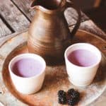 two ceramic cps of blackberry milk on a try wit some wild blackberries and a ceramic jug