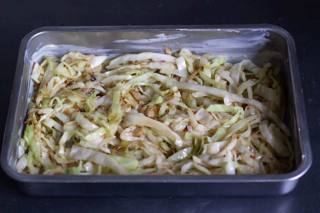 a stainless steel oven form with a layet of sliced and fried cabbage