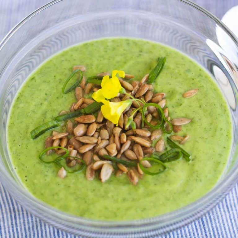 Chilled sorrel soup served in a small glass bowl and garnished with chopped spring onions, toasted and salted sunflower seeds and wood sorrel flowers.