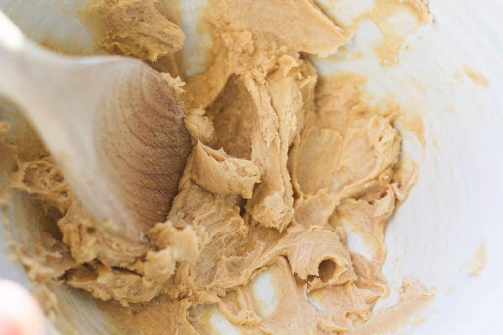 A wooden spoon creaming brown sugar and butter together in a ceramic white bowl