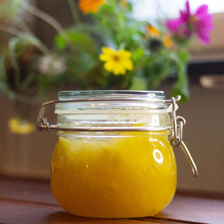 Garden marrow jam with lemon and ginger in a glass jar on a wooden table. There are garden flowers int he background
