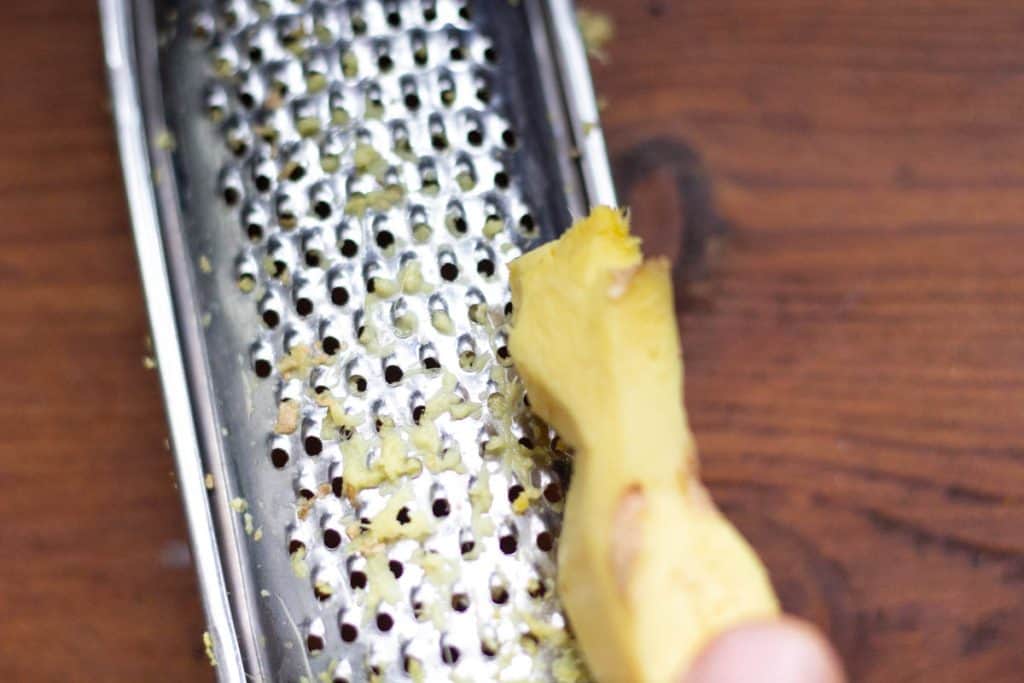 a hand grating some ginger root on a fine grater