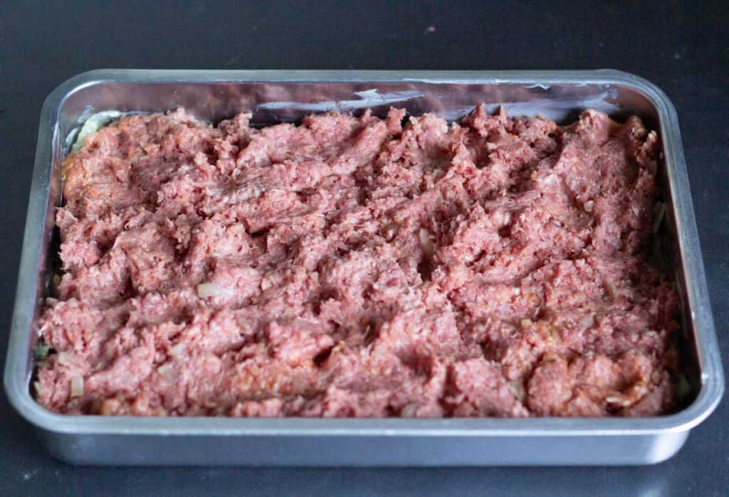 layer of meatloaf mixture on top of a layer of cabbage in a stainless steel oven form