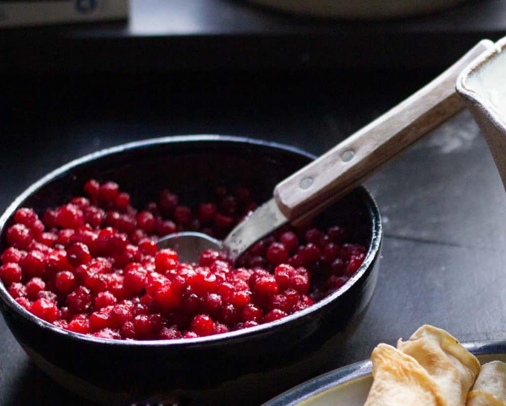 lingonberry sauce - also called rårörd lingon in a ceramic bowl beside swedish pancakes