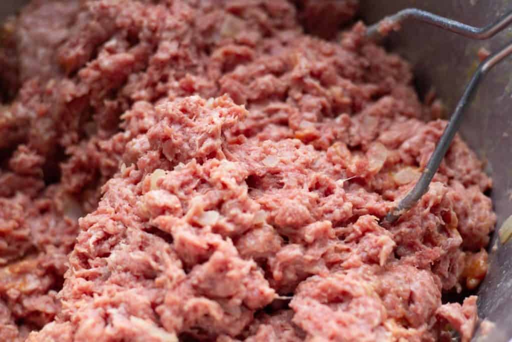 a potato masher mixing the meatloaf ingredients
