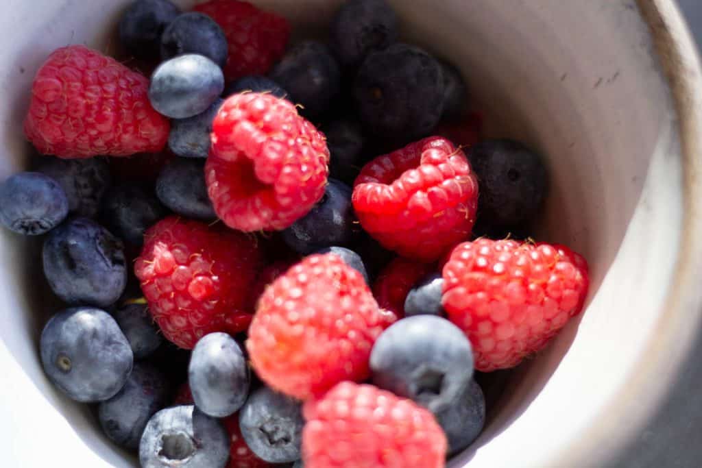 fresh raspberries and blueberries in a white ceramic bowl