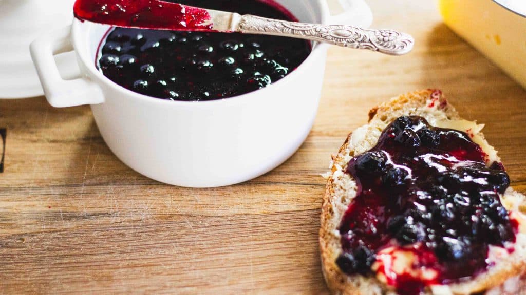 Queens Jam spread on toast with butter. There is a pot of jam beside the toast and a silver knife balanced on the pot.