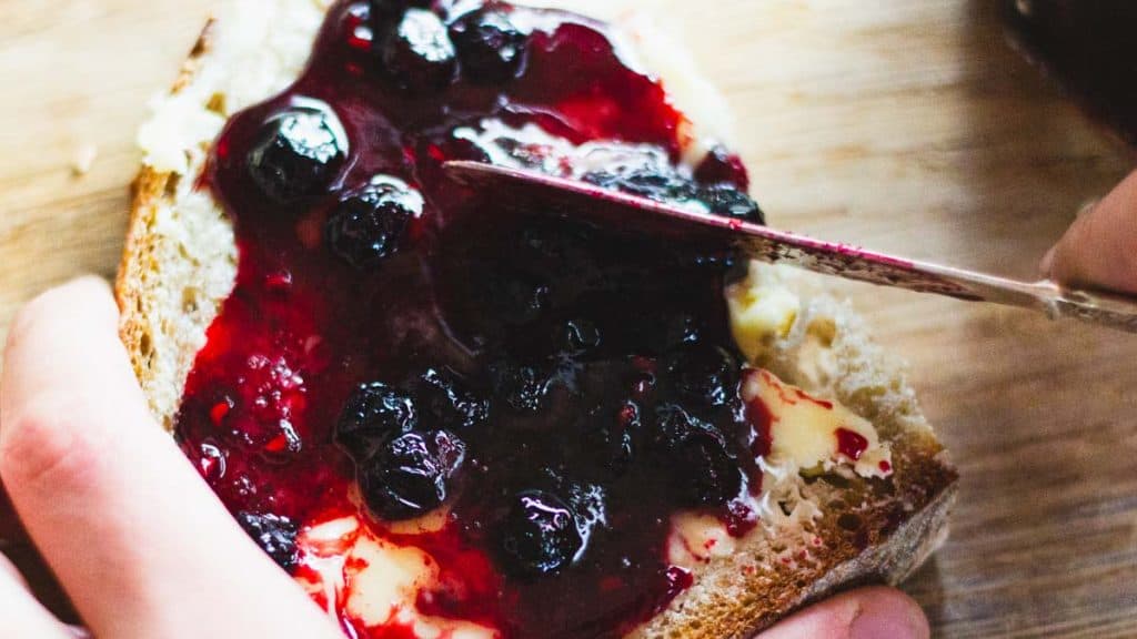 A knife spreading queens jam on a slice of bread