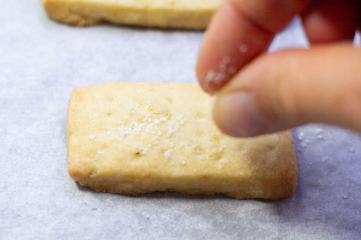 A hand sprinkling salt on a lemon shortbread cookie