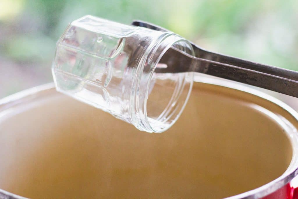 a tongs removing a glass jar from a pot of hot water
