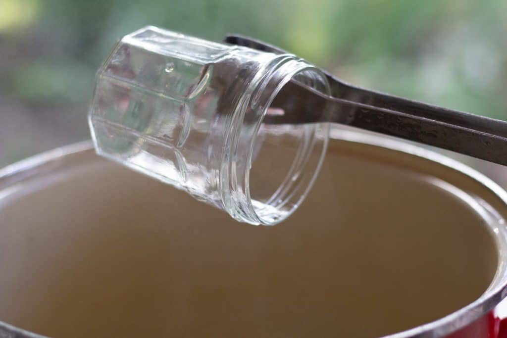 tongs removing a glas jar froma pot of boiling water