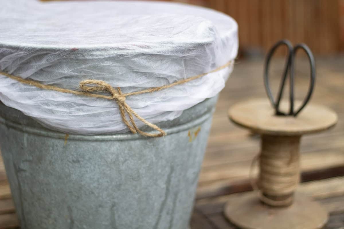 a metal bucket covered with gardners fleece which is tied with rustic string