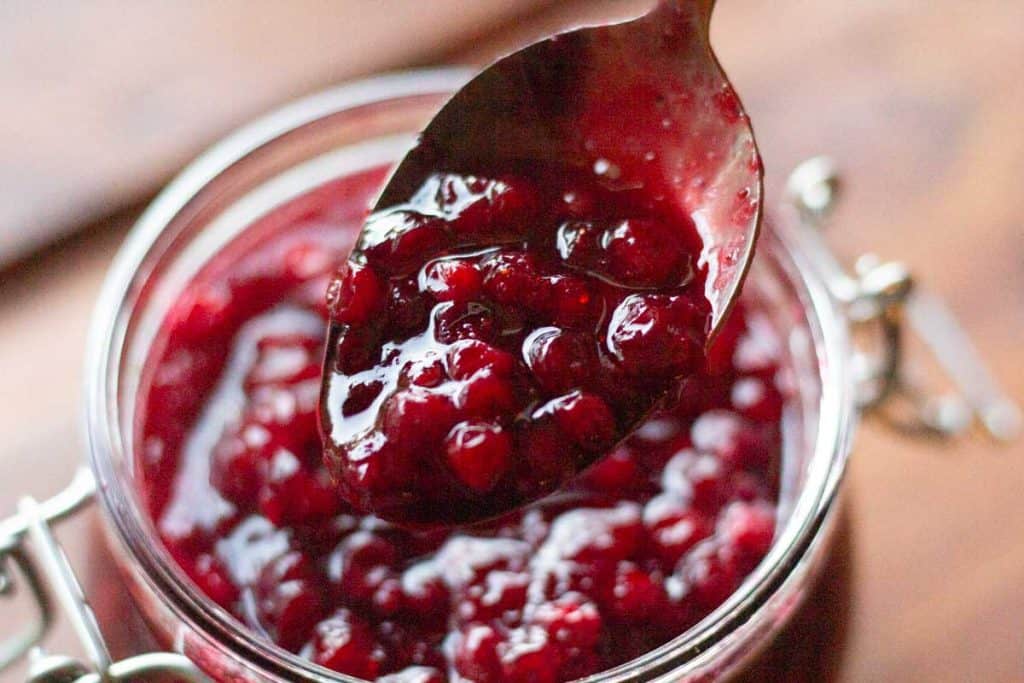 A spoon scooping lingonberry jam from a jar