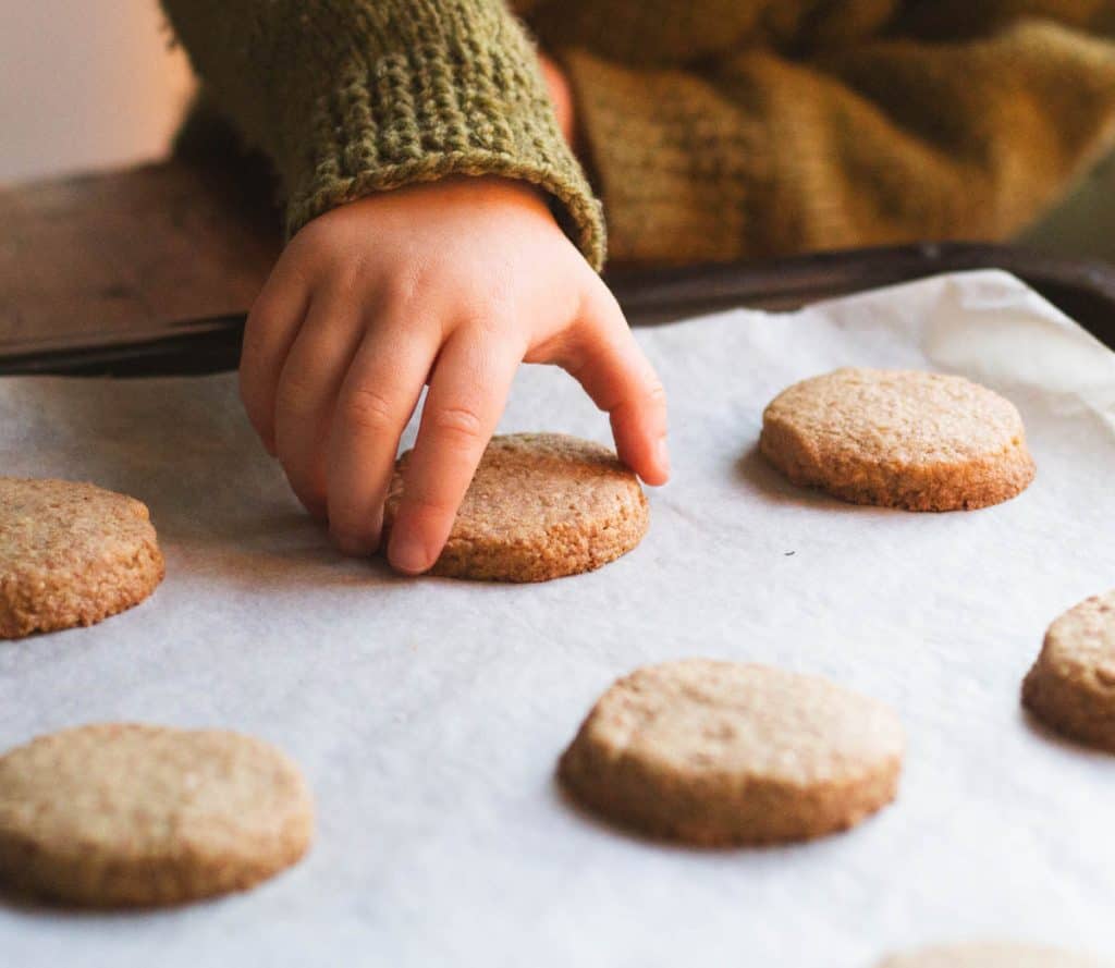 A child's hand picking up a whole wheat shortbread cookie from a cookie sheet