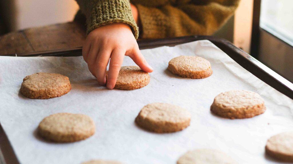 A child picking up a whole wheat shortbread cookie from a cookie sheet