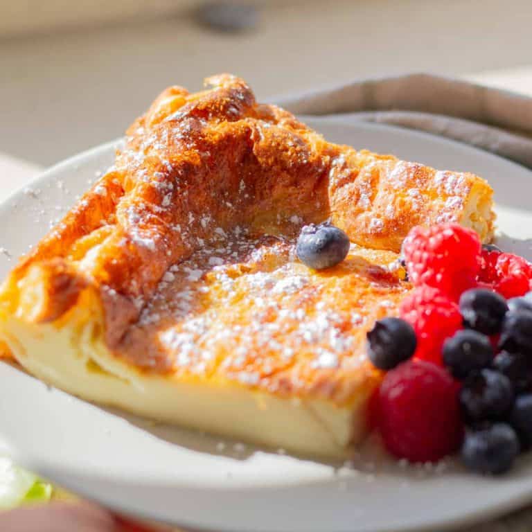 A slice of Swedish oven pancake served with a sprinkle of powdered sugar and fresh mixed berries
