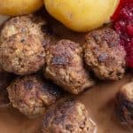 Swedish meatballs served beside boiled potatoes, lingonberry jam and cream sauce