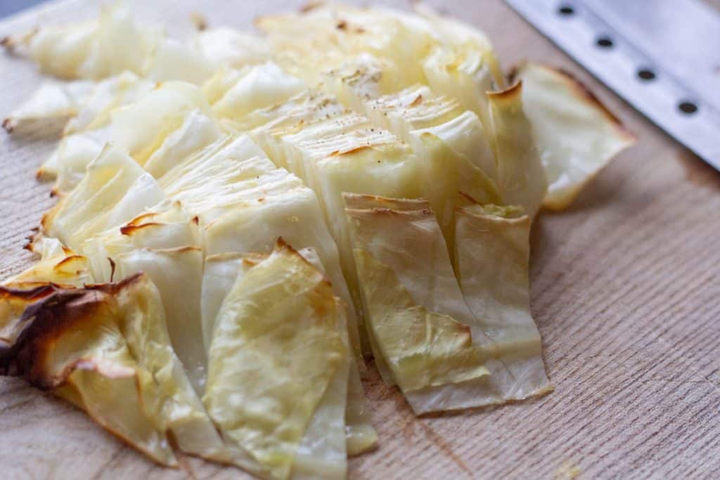 chopped roasted cabbage steaks on a chopping board beside a sharp knife