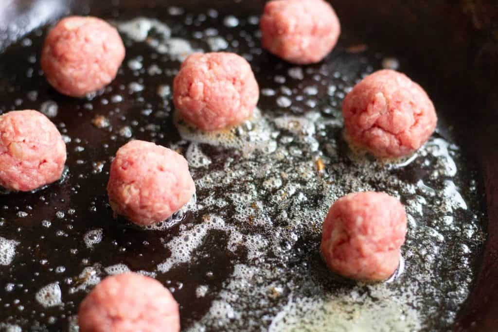 meatballs frying in a cast iron pan