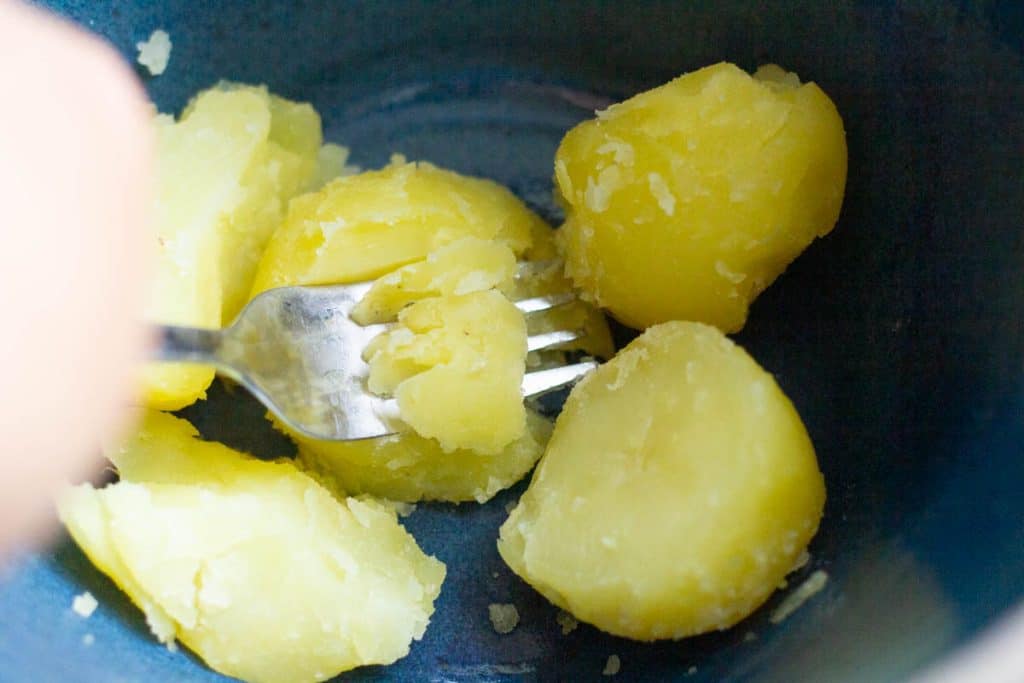 A fork mashing boiled potatoes in a large bowl