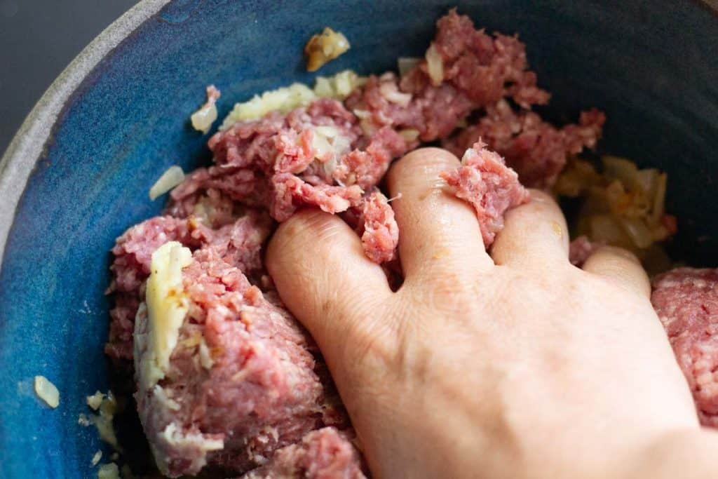 A hand mixing swedish meatball mixture