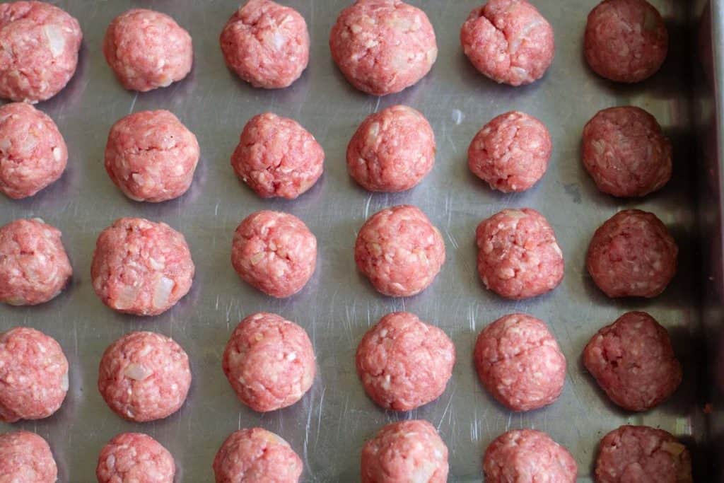 Swedish meatballs lined in a row on an oiled baking tray