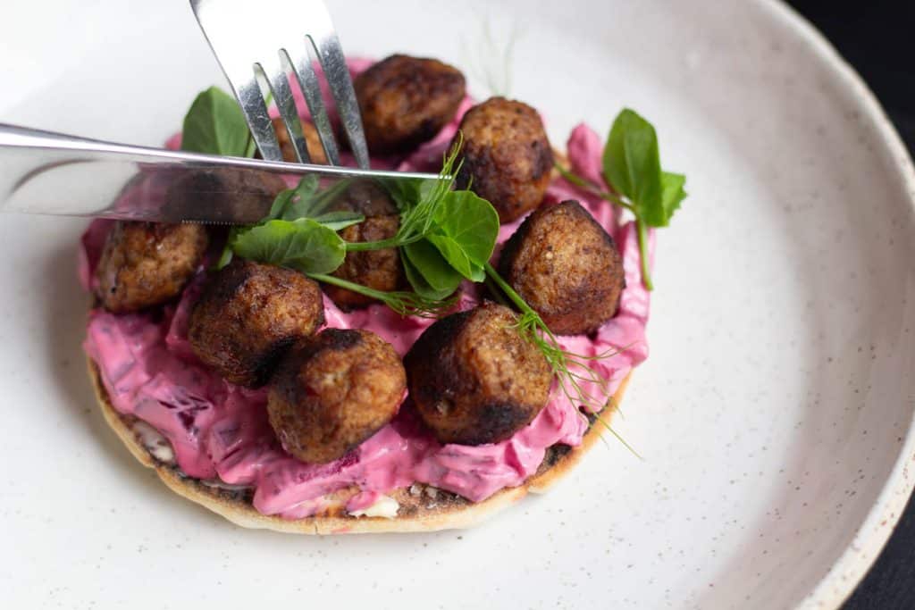 A knife and fork cutting into a Swedish Meatball Sandwich on a white ceramic plate