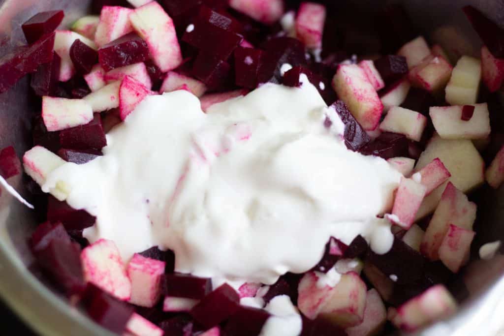 A large mixingbowl filled with finely chopped beetroot and finely chopped apple. On top is a creamy dressing