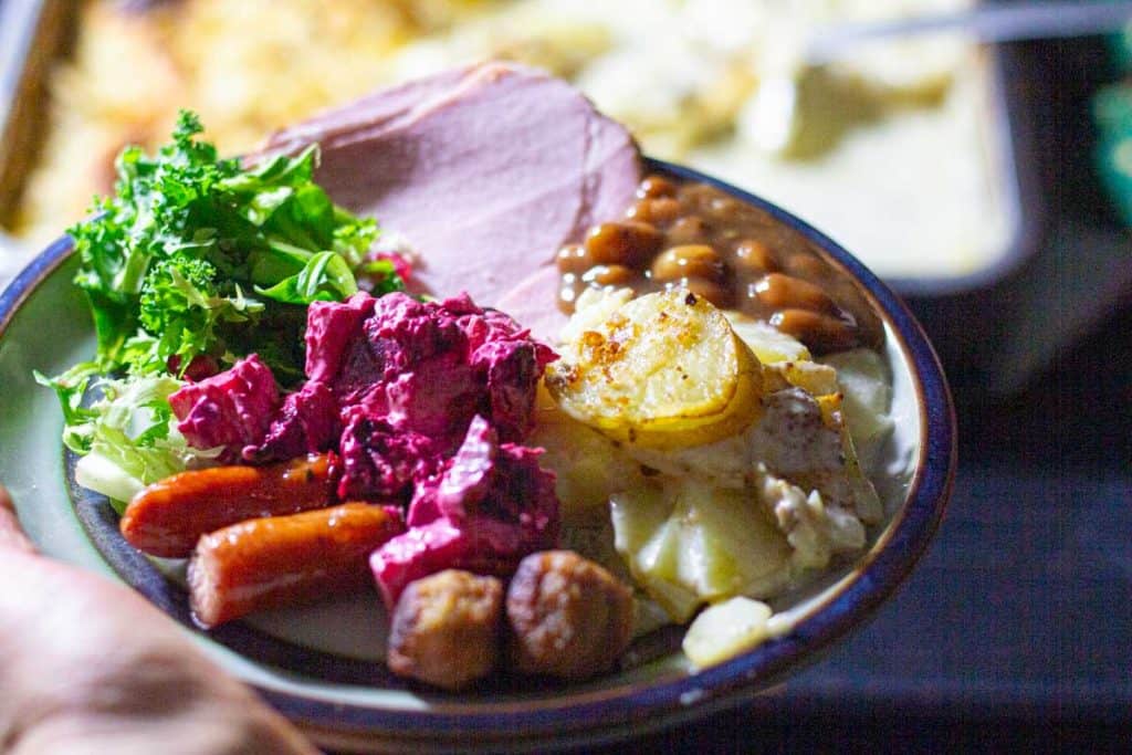 Swedish Christmas food on a ceramic plate. ( sausage, beetroot and apple salad, Janssons potato gratin, brown beans, salad, meatballs and smoked ham.)