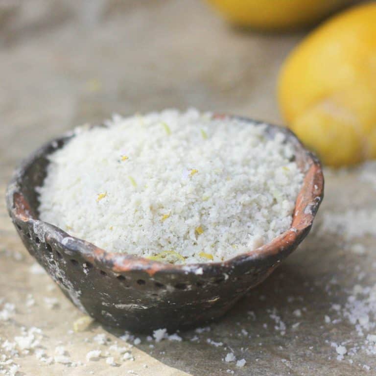 Lemon salt in a handmade pottery salt dish. There are fresh lemons in the background