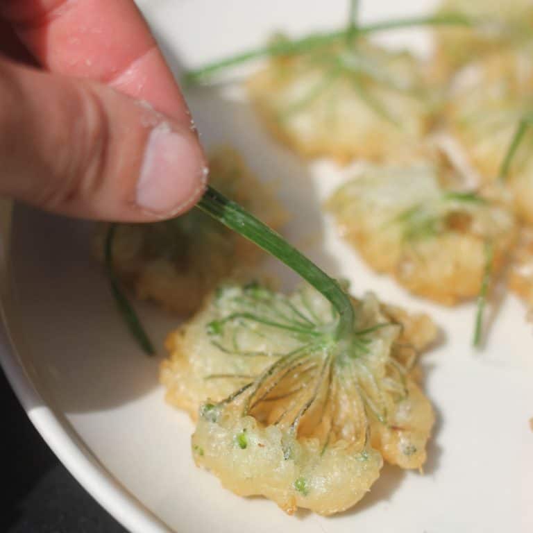 a hand picking up a wild garlic flower fritter by the stalk.