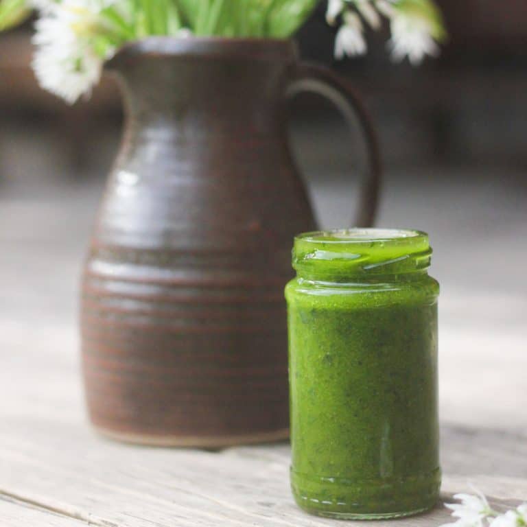 Wild garlic salad dressing in a little jar beside a jug of wild garlic flowers
