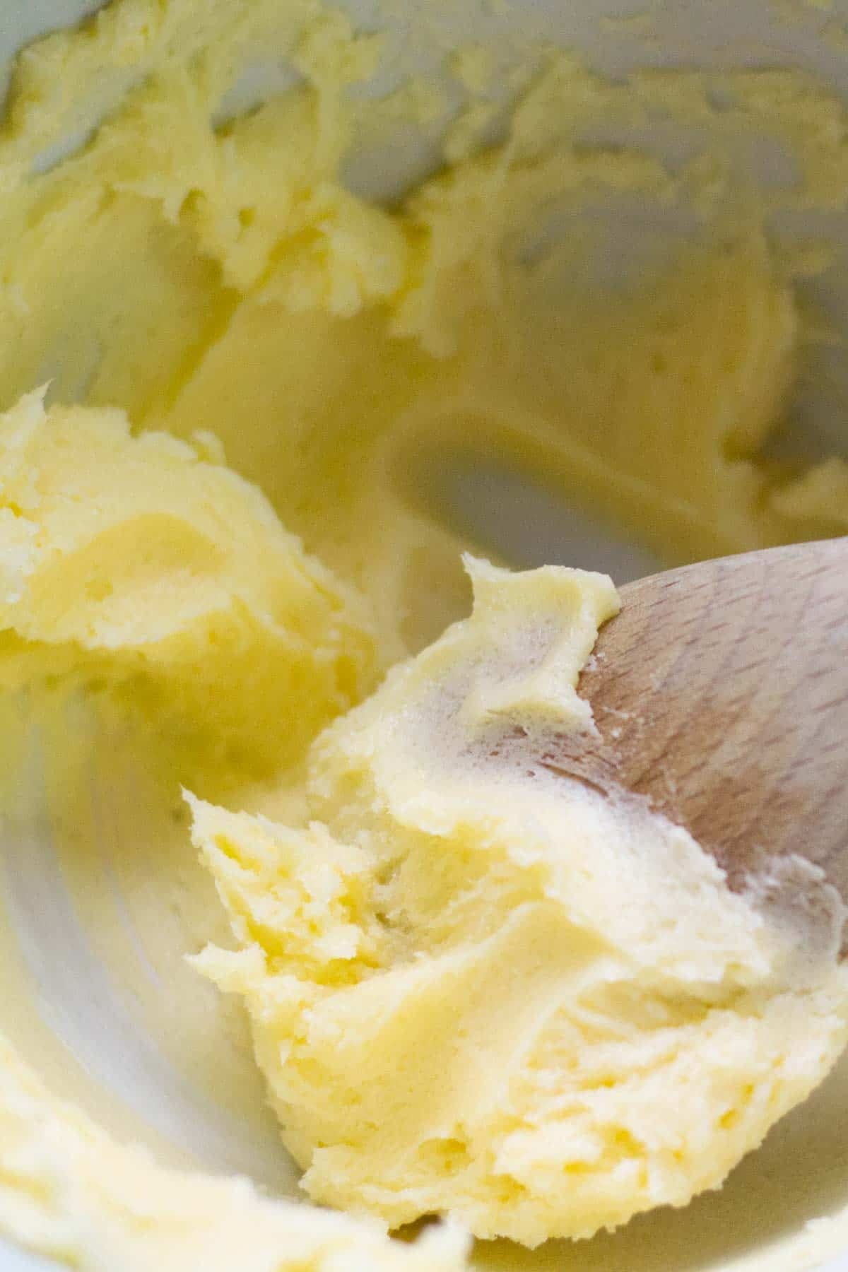 a wooden spoon creaming butter and sugar together in a white ceramic bowl