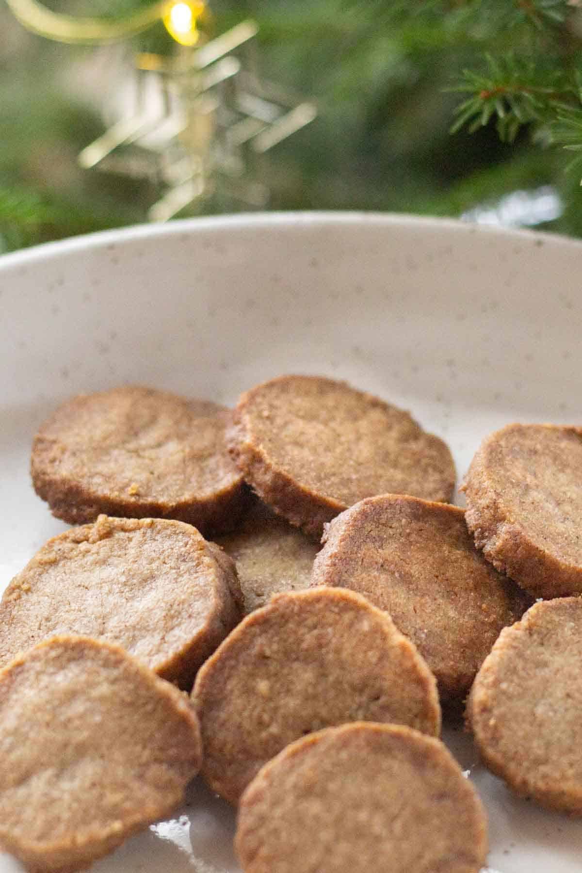 Round Gingerbread shortbread cookies on a white ceramic plate with christmas greenery in the background