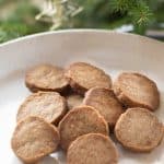 Round Gingerbread shortbread cookies on a hite ceramic plate with christmas greenery in the background