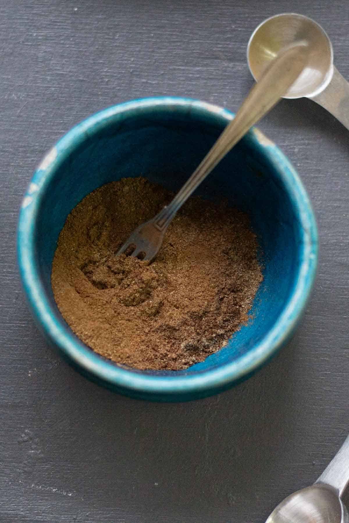 A small fork mixing Gingerbread spices in a blue ceramic bowl 