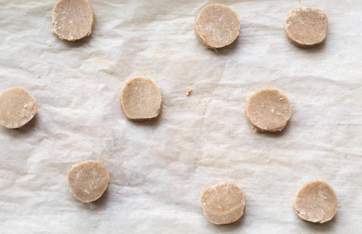 round slices of gingerbread shortbread dough on a baking sheet lined with parchment paper