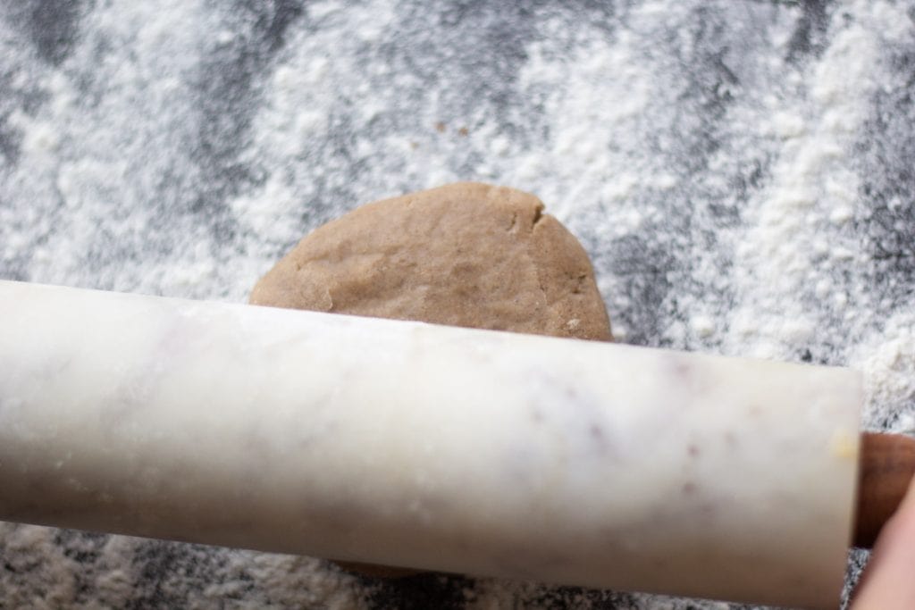 A rolling pin rolling a disc of  gingerbread short bread on a ightly floued surface
