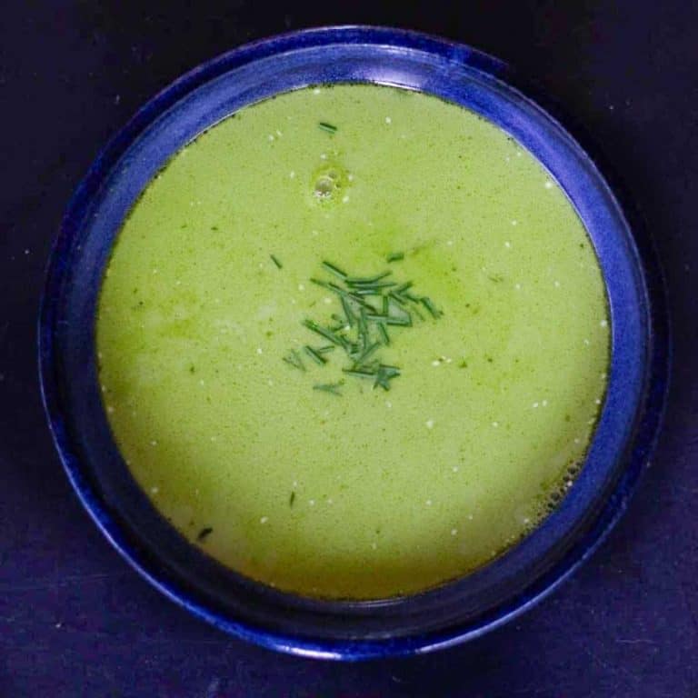 Fresh pea shoot soup in a dark blue ceramic bowl and garnished with chopped chives