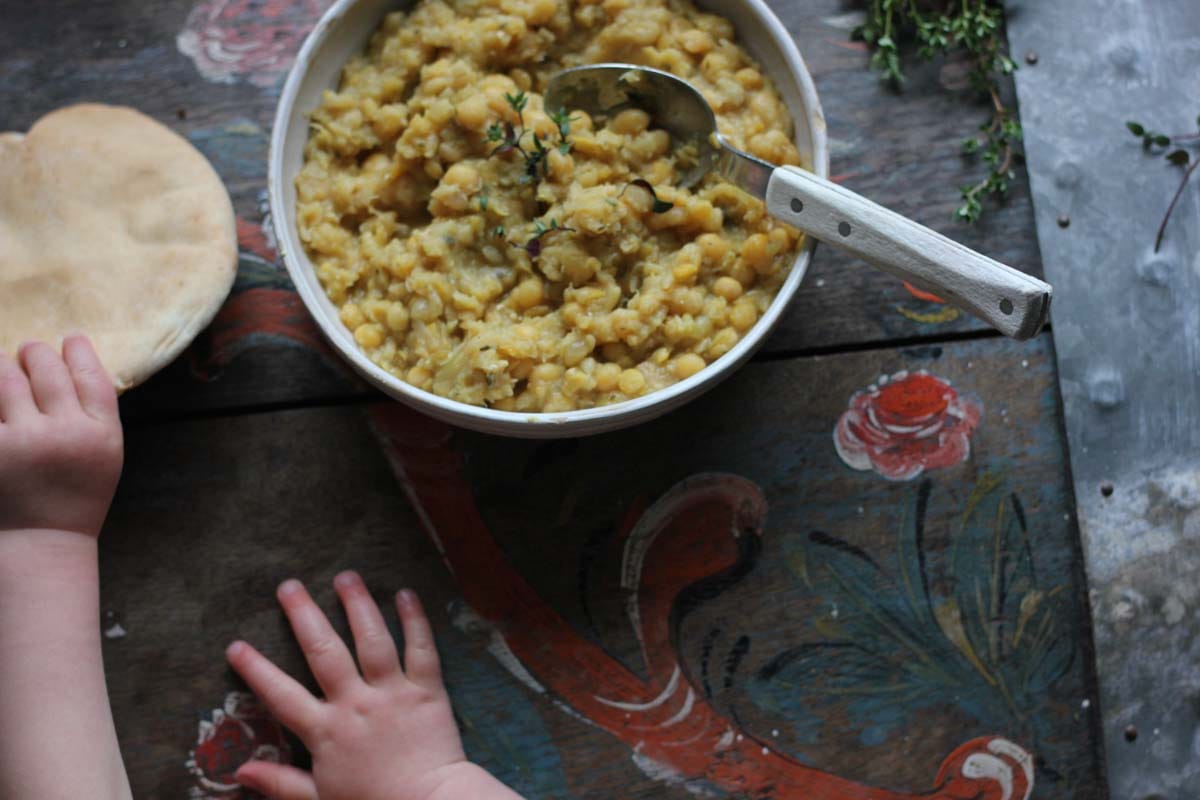 a childs hand taking a slice of bread to dip in a bowl of ärtsoppa