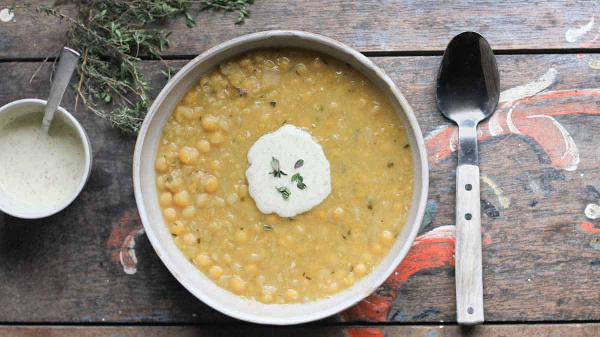 a white ceramic bowl filled with ärtsoppa, swedish pea soup topped with creamy mustard sauce adn fresh thyme.