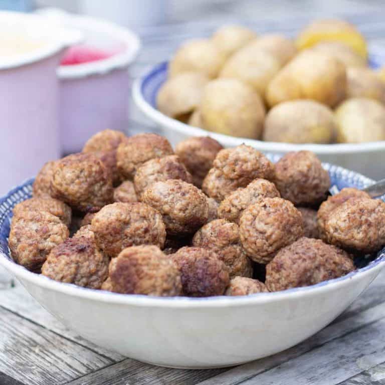 a ceramic bowl of swedish meatballs beside a bowl of boiled potatoes and a pot of lingonberry jam