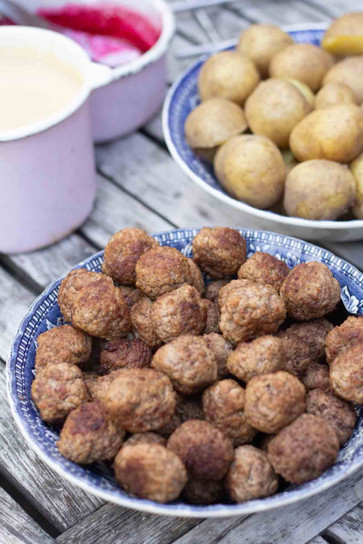 a bowl of swedish meatballs because a bowl of boiled potatoes and a pot of lingonberry jam and a pot of cream sauce